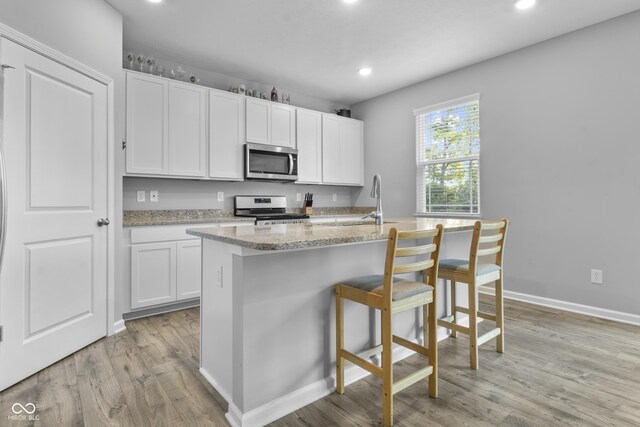 kitchen with white cabinetry, a kitchen island with sink, stove, and light wood-type flooring