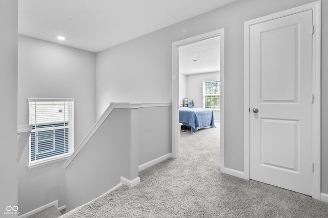 hallway featuring baseboards, light colored carpet, and an upstairs landing