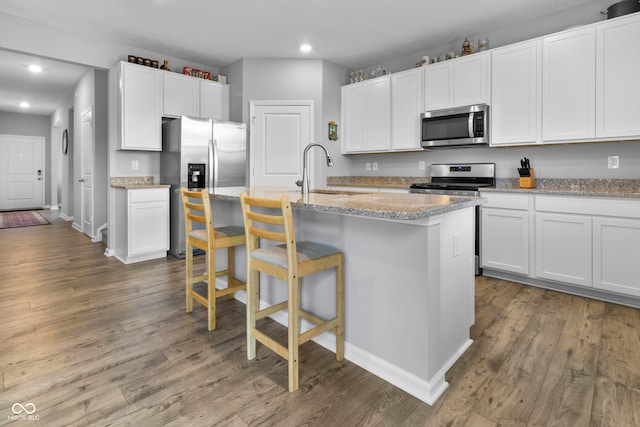 kitchen featuring light stone countertops, stainless steel appliances, a center island with sink, sink, and hardwood / wood-style flooring