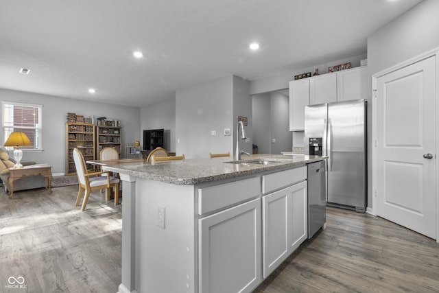 kitchen featuring dark wood finished floors, appliances with stainless steel finishes, white cabinetry, a sink, and an island with sink