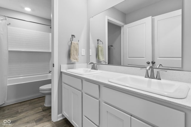 bathroom with toilet, double vanity, a sink, and wood finished floors