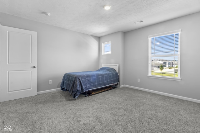 carpeted bedroom featuring a textured ceiling, visible vents, and baseboards