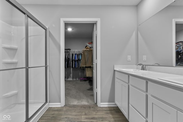 bathroom with baseboards, wood finished floors, a spacious closet, vanity, and a shower stall