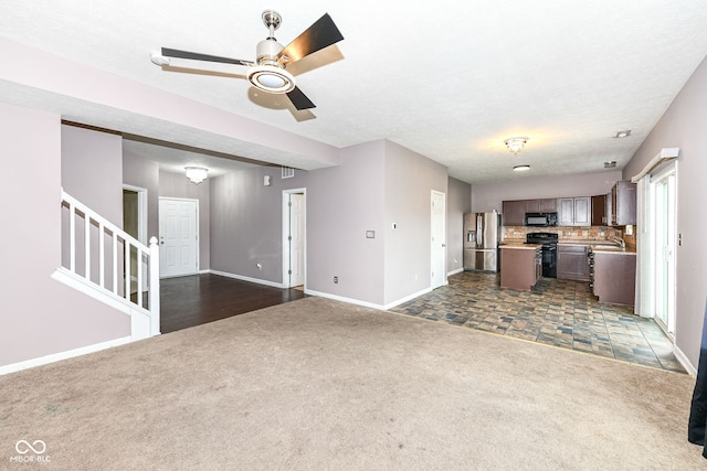 unfurnished living room featuring dark colored carpet, a textured ceiling, ceiling fan, and sink