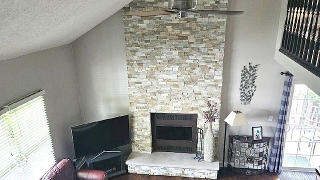 living room featuring vaulted ceiling, ceiling fan, a fireplace, and a textured ceiling