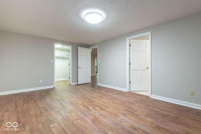 unfurnished bedroom with a closet, a walk in closet, a textured ceiling, and light hardwood / wood-style floors