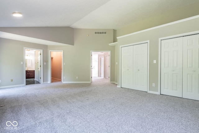 unfurnished bedroom with ensuite bath, two closets, vaulted ceiling, and carpet flooring