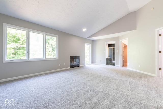 unfurnished living room with carpet flooring, a textured ceiling, vaulted ceiling, and plenty of natural light