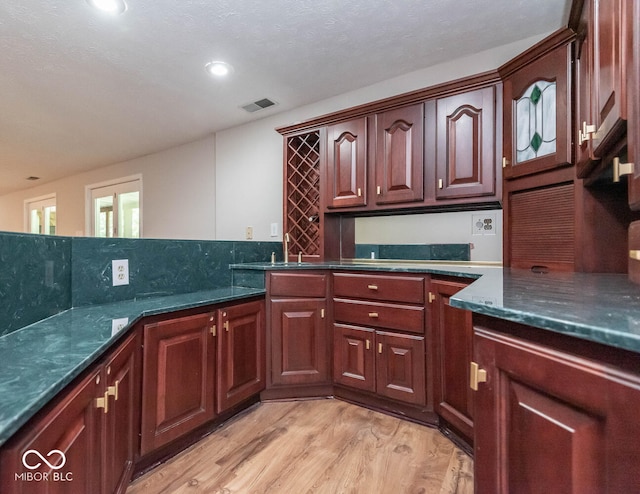 kitchen with sink, light wood-type flooring, dark stone countertops, and decorative backsplash