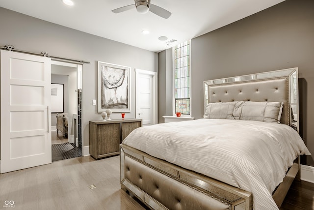 bedroom featuring ceiling fan, a barn door, and light hardwood / wood-style flooring