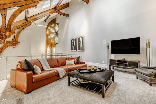 carpeted living room featuring beam ceiling, high vaulted ceiling, and a skylight