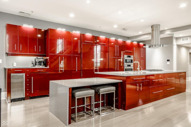 kitchen featuring paneled built in refrigerator, light stone countertops, an island with sink, island range hood, and stainless steel double oven