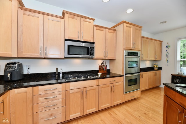 kitchen featuring light wood-type flooring, dark stone countertops, light brown cabinets, and stainless steel appliances