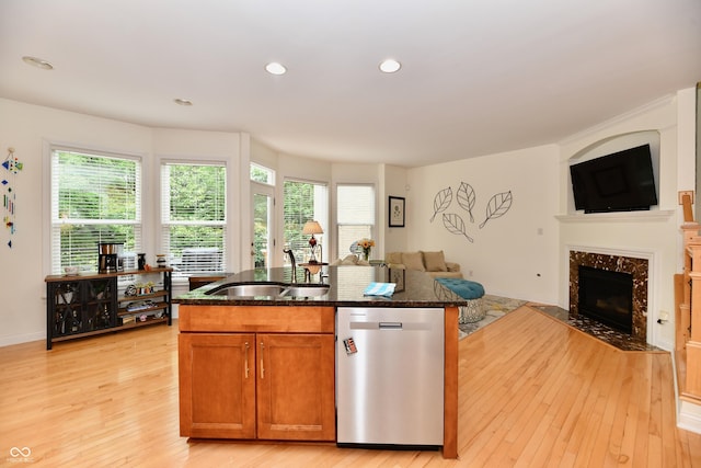 kitchen featuring dark stone counters, an island with sink, sink, stainless steel dishwasher, and light hardwood / wood-style flooring