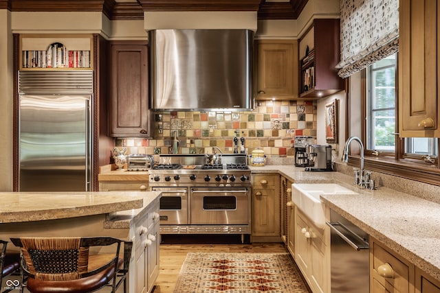 kitchen with sink, light hardwood / wood-style flooring, exhaust hood, light stone countertops, and high quality appliances