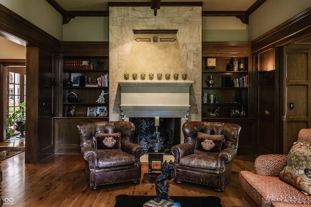 living room featuring wood-type flooring, a fireplace, crown molding, and built in shelves