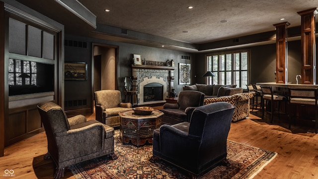 living room with light wood-type flooring, a textured ceiling, a fireplace, and ornate columns