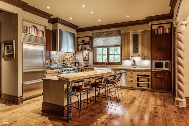 841 Alverna Dr, Indianapolis, IN 46260 - kitchen with built in appliances, wall chimney exhaust hood, ornamental molding, a kitchen breakfast bar, and light wood-type flooring