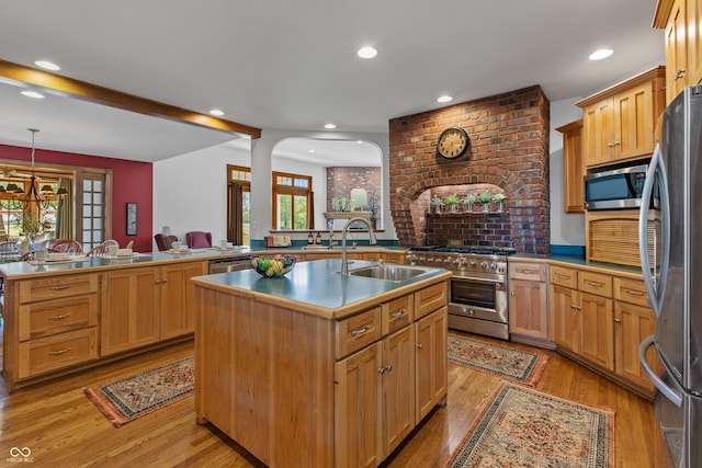 kitchen with appliances with stainless steel finishes, decorative light fixtures, a kitchen island with sink, and sink