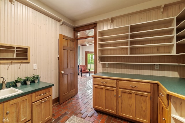 kitchen featuring ceiling fan, wooden walls, and sink