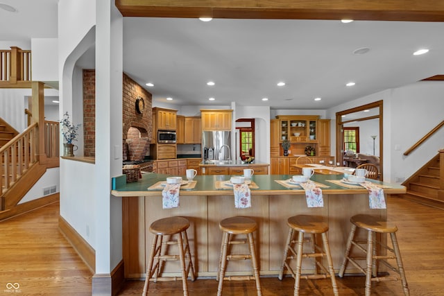 kitchen with sink, light wood-type flooring, a kitchen bar, kitchen peninsula, and stainless steel appliances