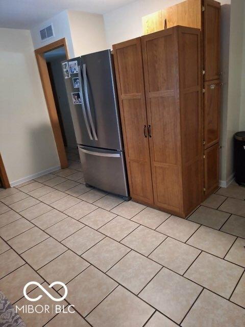 kitchen with brown cabinetry, freestanding refrigerator, visible vents, and light tile patterned flooring