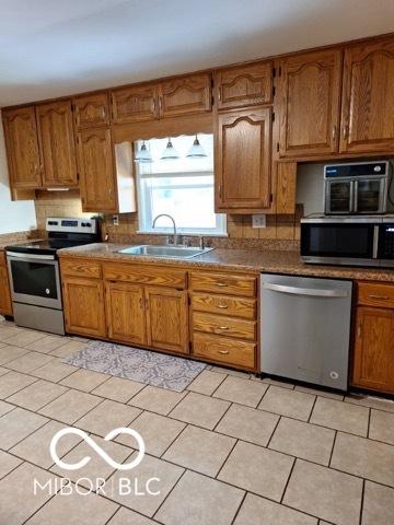 kitchen featuring brown cabinetry, decorative backsplash, dark countertops, stainless steel appliances, and a sink