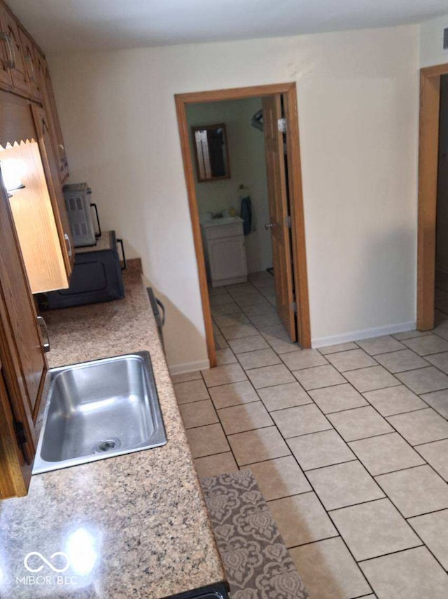 kitchen with light tile patterned floors, washer / clothes dryer, light countertops, a sink, and baseboards