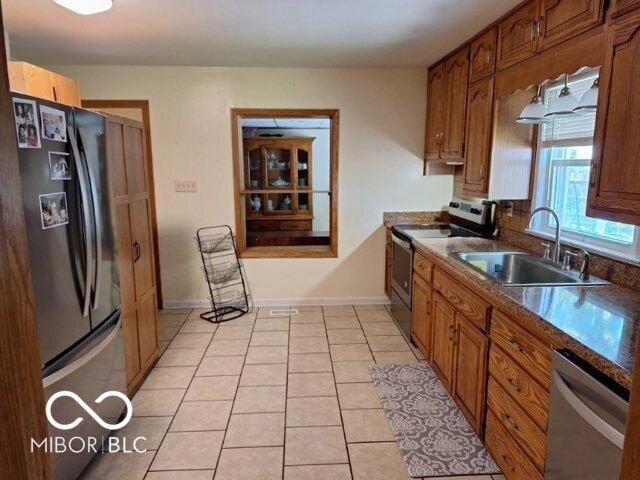 kitchen featuring brown cabinets, light tile patterned floors, stainless steel appliances, dark countertops, and a sink