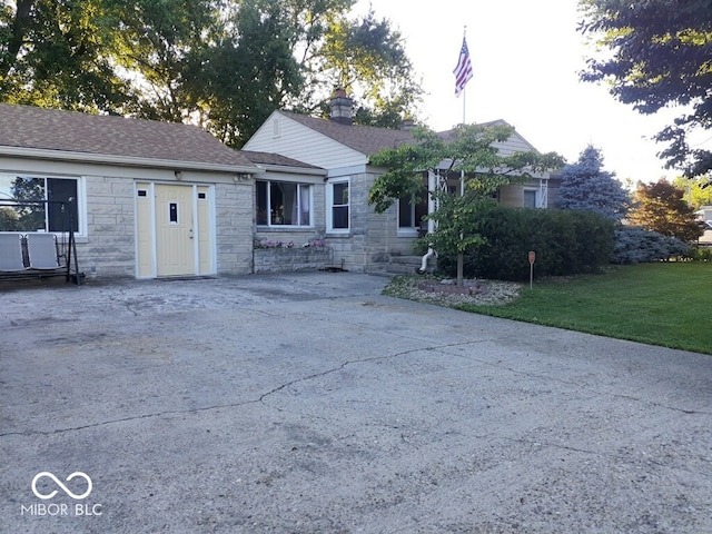 ranch-style home featuring a shingled roof, a front yard, stone siding, and concrete driveway