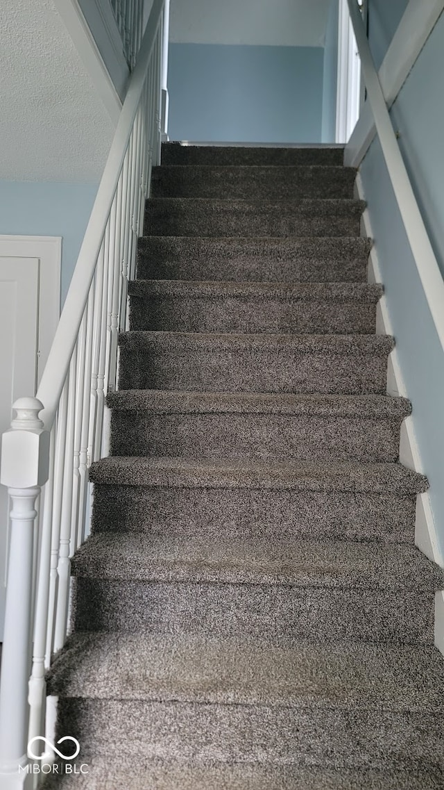 stairway featuring carpet flooring and a textured ceiling