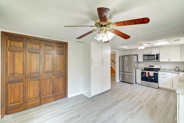 kitchen featuring light stone countertops, light wood-type flooring, stainless steel appliances, ceiling fan, and white cabinetry