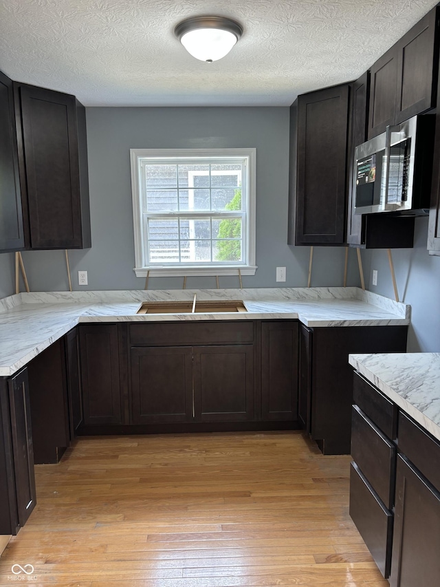 kitchen featuring sink, light hardwood / wood-style flooring, light stone countertops, a textured ceiling, and dark brown cabinets