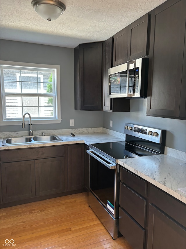 kitchen featuring light wood-type flooring, appliances with stainless steel finishes, a textured ceiling, and sink