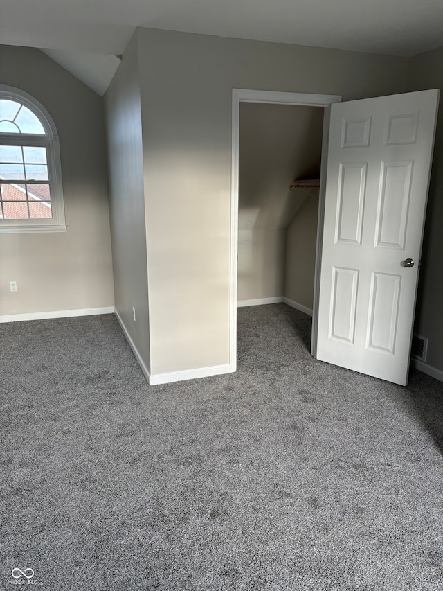 unfurnished bedroom with dark colored carpet, a closet, a spacious closet, and vaulted ceiling