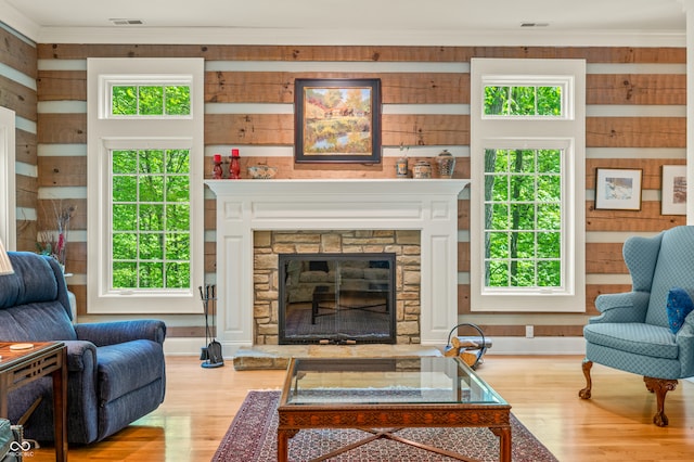 living room with a stone fireplace, wood walls, light hardwood / wood-style flooring, and ornamental molding