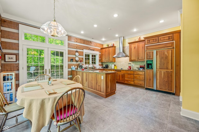 kitchen featuring paneled refrigerator, brown cabinets, a sink, crown molding, and wall chimney range hood