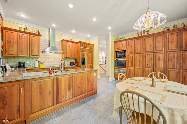 kitchen featuring light stone countertops, a peninsula, decorative backsplash, built in appliances, and wall chimney exhaust hood