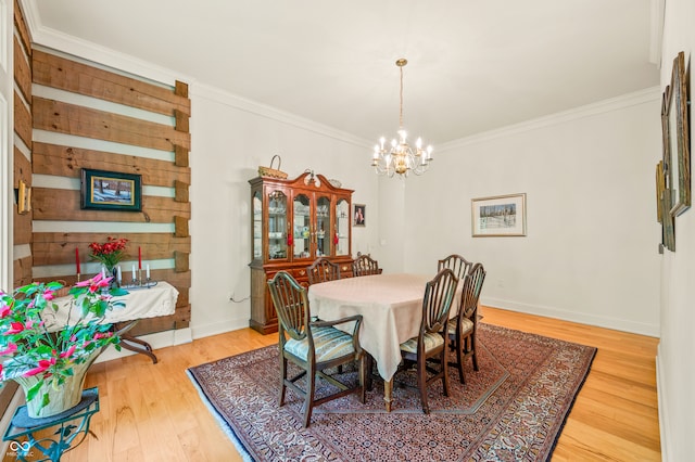 dining space with a notable chandelier, wooden walls, light wood-type flooring, and ornamental molding