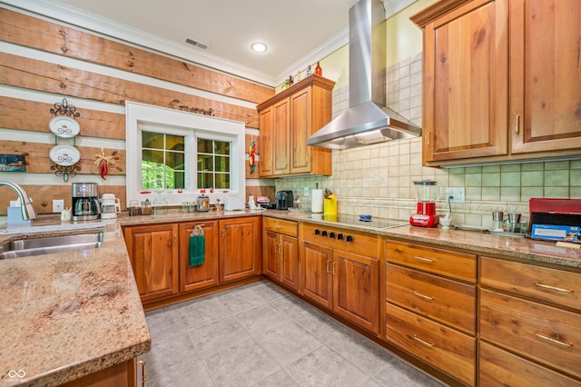 kitchen featuring a sink, light stone counters, crown molding, and wall chimney range hood