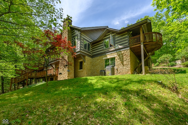 rear view of property with central air condition unit, a balcony, a lawn, and a wooden deck