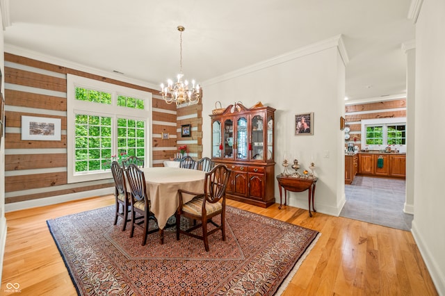 dining space featuring light hardwood / wood-style floors, a notable chandelier, crown molding, and wooden walls