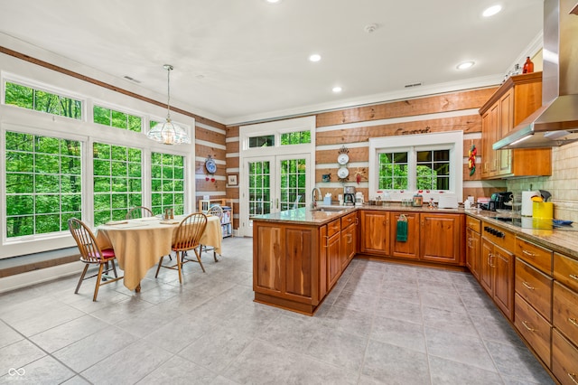 kitchen featuring kitchen peninsula, a wealth of natural light, light stone countertops, and wall chimney range hood