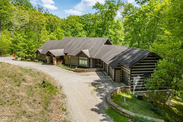 log cabin with a wooded view and dirt driveway