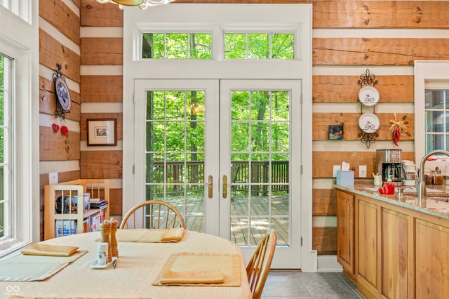 tiled dining area featuring french doors, wooden walls, and a healthy amount of sunlight