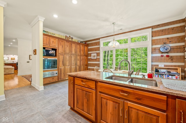 kitchen with built in microwave, wooden walls, sink, light stone countertops, and light hardwood / wood-style floors