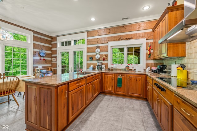 kitchen with light tile patterned flooring, wood walls, light stone countertops, and wall chimney exhaust hood