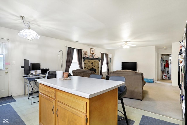 kitchen featuring ceiling fan with notable chandelier, pendant lighting, a center island, a fireplace, and a kitchen breakfast bar