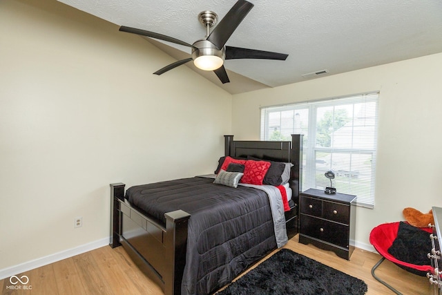 bedroom with ceiling fan, light wood-type flooring, vaulted ceiling, and a textured ceiling