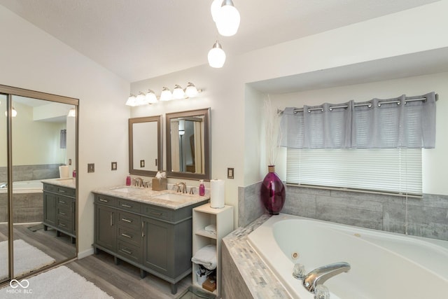 bathroom featuring lofted ceiling, wood-type flooring, vanity, and a relaxing tiled tub